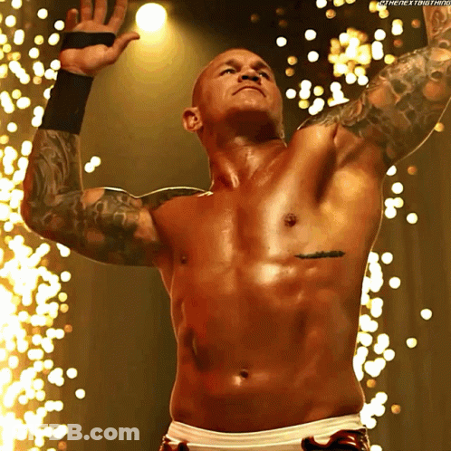 A Shirtless Wrestler With A Tattoo On His Chest Stands In Front Of Sparks GIF