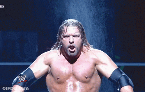 A Shirtless Wrestler With A W Logo On His Arm Stands In Front Of A Waterfall GIF