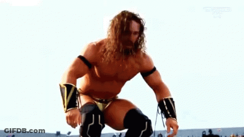 A Shirtless Wrestler With Long Hair And A Beard Is Kneeling Down On A Ring . GIF