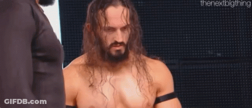 A Shirtless Wrestler With Long Hair And A Beard Is Standing In Front Of A Large Screen . GIF