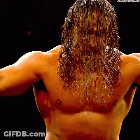 A Shirtless Wrestler With Long Hair Is Standing In The Dark . GIF