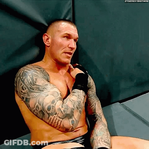 A Shirtless Wrestler With Tattoos On His Arms Is Sitting On The Floor GIF