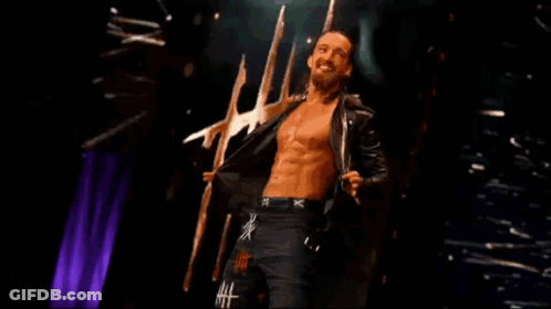 A Shirtless Wrestler With The Letter X On His Shorts Is Standing On A Stage GIF
