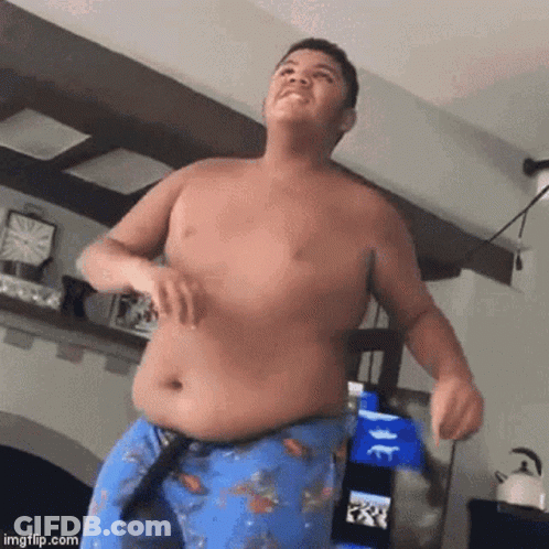 A Shirtless Young Man Is Dancing In A Living Room While Wearing Blue Shorts . GIF