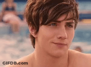 A Shirtless Young Man Is Standing In Front Of A Swimming Pool Looking At The Camera . GIF