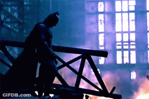 A Silhouette Of A Man In A Batman Costume Stands On A Bridge GIF