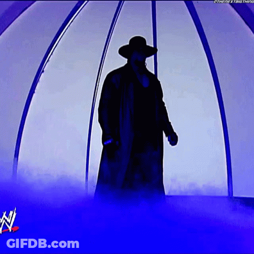 A Silhouette Of A Man In A Trench Coat And Hat Standing In A Tunnel With A W Logo In The Background GIF