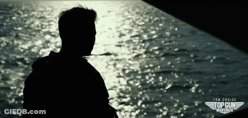 A Silhouette Of A Man Standing In Front Of A Body Of Water With The Words Tom Cruise Top Gun Maverick On The Bottom GIF