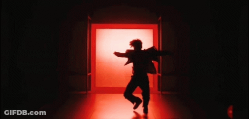 A Silhouette Of A Person In A Dark Room With Red Lights Behind Them GIF
