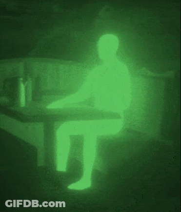A Silhouette Of A Person Sitting At A Table In A Dark Room With A Green Light Behind Them . GIF