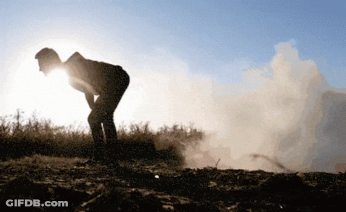 A Silhouette Of A Person Standing In A Field With Smoke Coming Out Of The Ground GIF