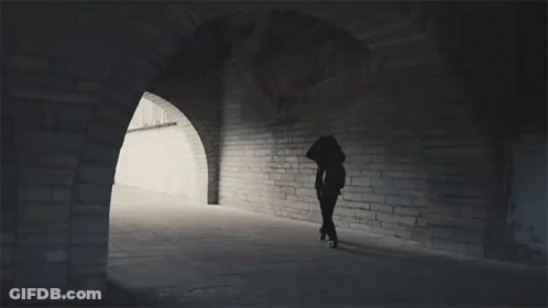 A Silhouette Of A Person Walking Through A Tunnel With Arches GIF