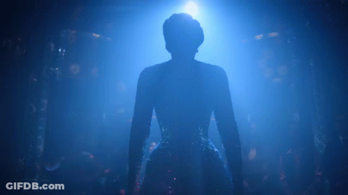 A Silhouette Of A Woman In A Blue Dress Is Standing In A Dark Room . GIF