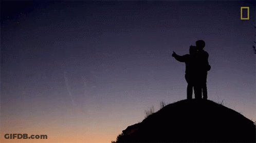 A Silhouette Of Two People Standing On Top Of A Hill GIF