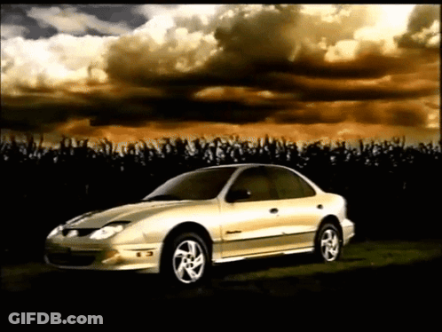 A Silver Car Is Parked In A Field With A Cloudy Sky Behind It GIF