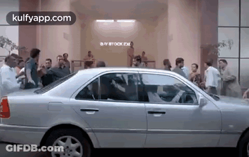 A Silver Car Is Parked In Front Of A Building With A Crowd Of People Standing Around It . GIF