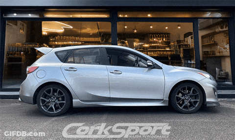 A Silver Corksport Car Is Parked In Front Of A Building GIF