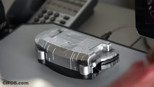 A Silver Item With The Letter D On It Sits On A Desk Next To A Phone GIF