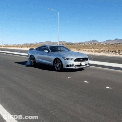 A Silver Mustang Is Driving Down A Desert Road GIF