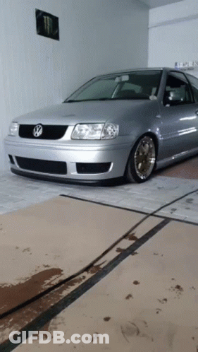 A Silver Volkswagen Is Parked In A Garage With A Monster Poster On The Wall Behind It GIF