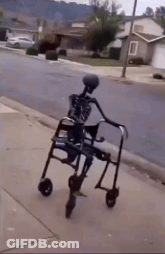 A Skeleton In A Walker Is Walking Down The Sidewalk . GIF