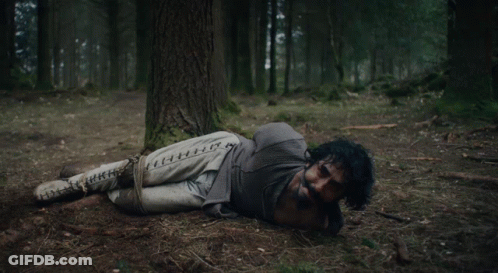 A Skeleton Laying Under A Tree In A Forest GIF
