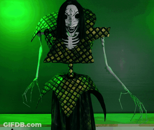 A Skeleton With Long Black Hair And Sharp Teeth Stands In Front Of A Green Wall GIF