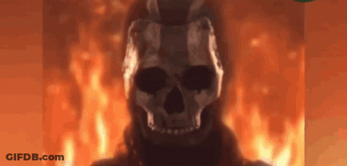A Skull Is Standing In Front Of A Fire In A Dark Room . GIF