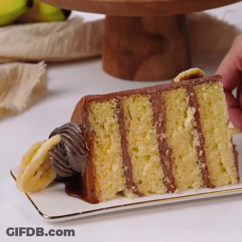 A Slice Of Banana Cake With Chocolate Frosting On A Plate GIF