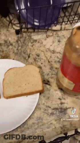 A Slice Of Bread On A Paper Plate Next To A Jar Of Peanut Butter GIF