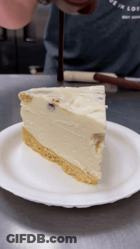 A Slice Of Cheesecake On A Paper Plate With A Person In The Background GIF