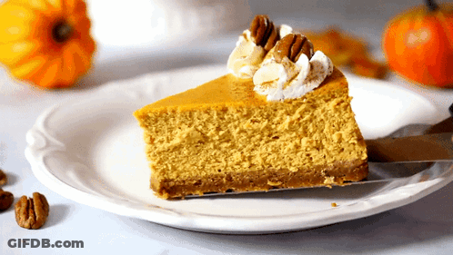 A Slice Of Pumpkin Cheesecake With Whipped Cream And Pecans On A White Plate GIF