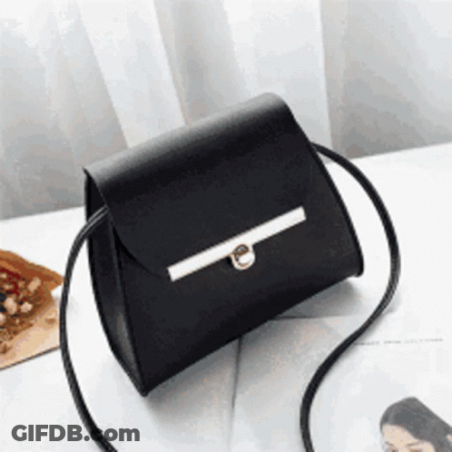 A Small Black Purse Is Sitting On A Table Next To A Magazine GIF