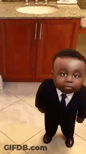 A Small Boy In A Suit And Tie Is Standing In Front Of A Bathroom Sink . GIF