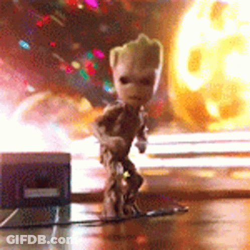 A Small Figurine Of Groot Is Standing On A Table In Front Of A Fireball . GIF