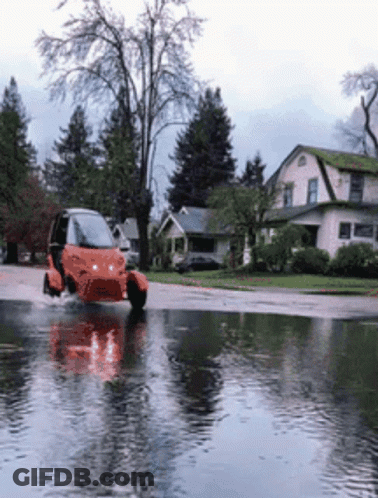 A Small Orange Vehicle Is Driving Through A Flooded Street GIF