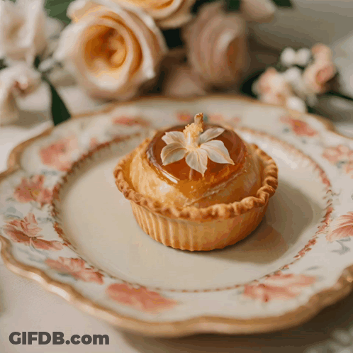 A Small Pastry With A Flower On Top Is On A Floral Plate GIF