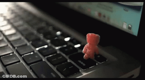 A Small Red Teddy Bear Sits On The Delete Key On A Laptop Keyboard GIF