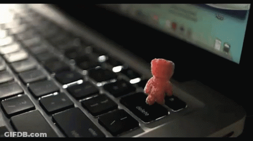 A Small Red Teddy Bear Sits On The Delete Key On A Laptop Keyboard GIF