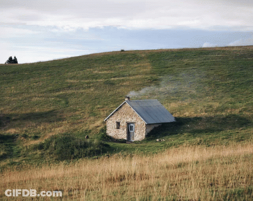 A Small Stone House Sits On Top Of A Grassy Hillside GIF