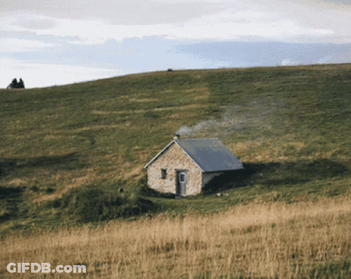 A Small Stone House Sits On Top Of A Grassy Hillside GIF