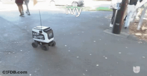 A Small White And Black Food Delivery Vehicle Is Driving Down A Street GIF