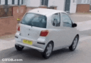 A Small White Car Is Parked On The Side Of The Road With A Yellow Plate GIF