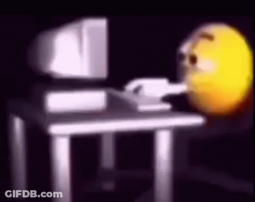 A Smiley Face Is Sitting At A Desk In Front Of A Computer Monitor . GIF