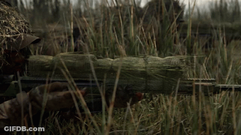 A Sniper Is Standing In The Grass With A Rifle In His Hand GIF