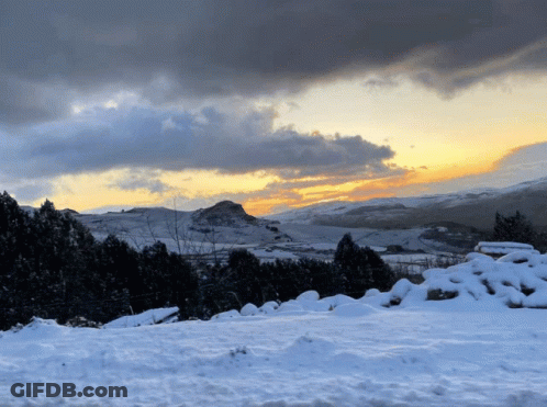 A Snowy Hillside With A Mountain In The Background GIF