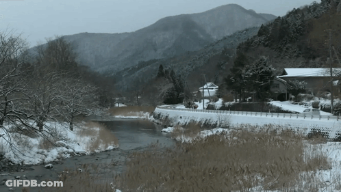 A Snowy River With Mountains In The Background And A House In The Foreground GIF