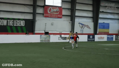 A Soccer Game Is Being Played In An Indoor Stadium With A Cane 'S Sign On The Wall GIF