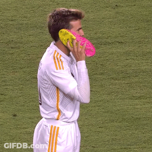 A Soccer Player Has A Pair Of Pink And Yellow Soccer Cleats On His Face GIF