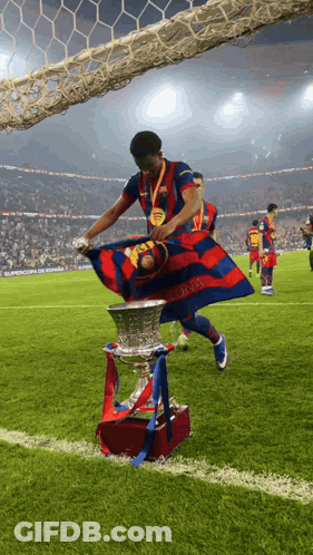 A Soccer Player Holds A Trophy And A Flag That Says Barcelona GIF